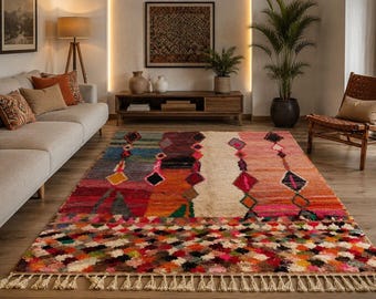 May include: A rectangular area rug featuring a vibrant, multi-colored geometric pattern with diamonds and stripes in shades of pink, orange, red, blue, and cream. The rug has a textured pile, a repeating diamond border, and cream-colored fringe.