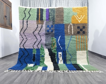 May include: A colorful, abstract rug with geometric patterns in shades of blue, green, purple, yellow, and brown. The rug has a fringe border.