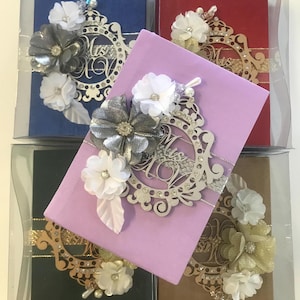 May include: A collection of boxed notebooks in various colors: blue, red, purple, green, and brown. Each notebook is adorned with a decorative floral arrangement and a laser-cut embellishment that reads "Mrs."