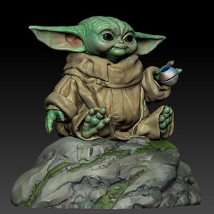 May include: A green and brown figurine of a character from the Star Wars franchise, sitting on a rock with a small sphere in its hand.