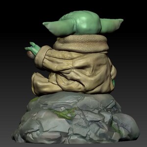 May include: A green and brown figurine of a character from the Star Wars franchise sitting on a rock. The character is wearing a brown jacket and has large ears.