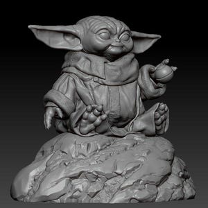 May include: A gray, 3D printed figurine of a character from the Star Wars franchise, sitting in a meditative pose on a rocky base. The character has large ears, a green skin tone, and is holding a small, round object in one hand.