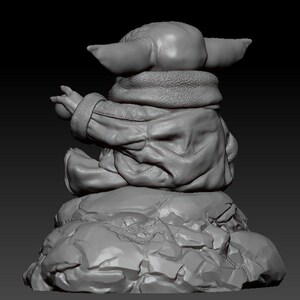 May include: A gray 3D printed figurine of a character from the Star Wars franchise, sitting on a rocky base. The character is wearing a hooded jacket and has large ears.