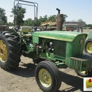 以下が含まれることがあります： 大きな黒いタイヤと黄色のリムが付いた緑色のジョンディアトラクター。 トラクターにはロールバーがあり、フードには「JOHN DEERE」の文字が見えます。 トラクターは晴れた日に屋外にあります。