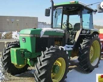 May include: A green John Deere 2355 tractor with large black tires and yellow rims. The tractor has a cab with glass windows and a steering wheel. Snow is visible on the tractor's roof and hood. The tractor is parked outdoors.