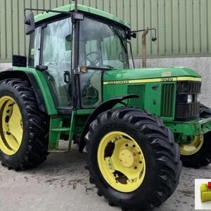 May include: A green John Deere 6010 tractor with large black tires and yellow rims. The tractor has a glass enclosed cab and the John Deere logo is visible on the front.