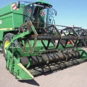 Könnte beinhalten: Ein grüner John Deere Mähdrescher mit einem großen Frontmähwerk und einer Kabine. Die Maschine hat große Reifen und ist für die Ernte von Feldfrüchten konzipiert. Der Mähdrescher steht draußen an einem sonnigen Tag.