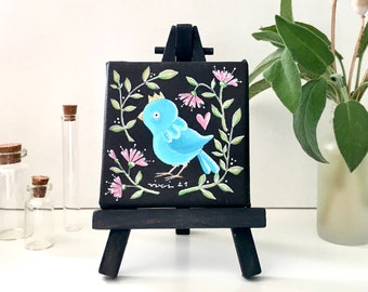 Tiny original decorative painting of a blue bird on black background with floral wreath - Small painting on easel, ready to display on shelf