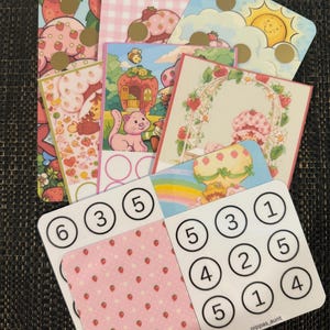 May include: A selection of illustrated cards with strawberry and gingham designs, and cartoon characters. Some cards display numbers within circles. One card has the text "pippas_aunt".