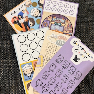 May include: A selection of colourful Friends-themed cards. One card features the show's logo and cast, while others display illustrations of characters, Central Perk, and a "Smelly Cat" design. The cards have various designs and numbers.