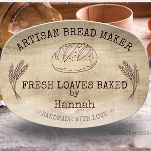 May include: Wooden sign with the text "ARTISAN BREAD MAKER" and "FRESH LOAVES BAKED by Hannah HANDMADE WITH LOVE". The sign features a bread illustration and wheat stalks. Eggs and baking supplies are in the background.