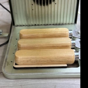 May include: Three wooden handles with metal attachments, arranged in a row on a metal surface. The handles are light brown and have a smooth finish.