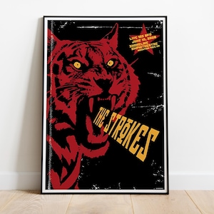 May include: Framed poster with a red tiger illustration and yellow eyes on a black background. The text "THE STROKES" in yellow is displayed. Additional text at the top indicates a live performance date and venue.