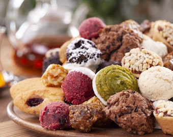 May include: A variety of cookies and pastries on a wooden platter. The cookies are in various shapes and colors, including chocolate, green, and red. There are also some cookies with nuts and sprinkles.