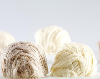 May include: Close-up of five white and brown cotton candy balls. The cotton candy is arranged in a row on a white surface.