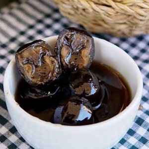 Può includere: Una ciotola bianca piena di metà noci marroni scure in uno sciroppo dolce. La ciotola è su una tovaglia a scacchi bianchi e neri.