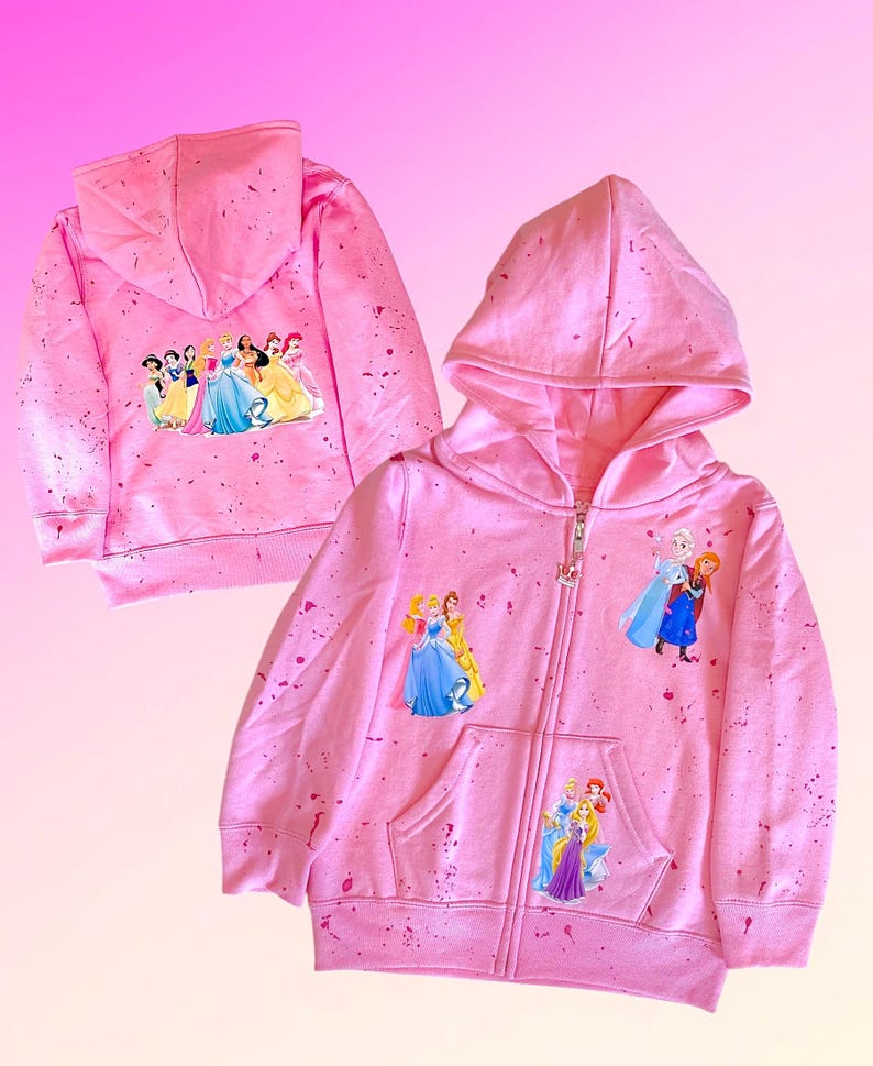 K&ouml;nnte beinhalten: Rosaer Kinder-Rei&szlig;verschluss-Hoodie mit Spr&uuml;hfarben-Design. Der Hoodie zeigt verschiedene Disney-Prinzessinnen auf der Vorder- und R&uuml;ckseite.