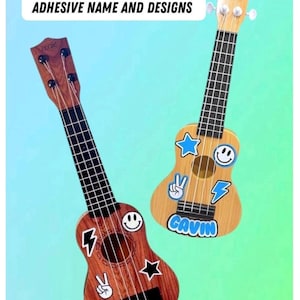 May include: Two mini plastic toy guitars with wood-grain finishes, black fretboards, and white tuning pegs. The guitars feature adhesive designs including stars, lightning bolts, smiley faces, and peace signs, with the names THEO and GAVIN printed.
