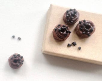 Peut inclure: Miniatures de pâtisseries au chocolat avec des pépites de chocolat noir sur une surface en bois brun clair. Trois pâtisseries sont disposées sur la surface, avec une pâtisserie séparée et quelques pépites de chocolat éparpillées à proximité. Les pâtisseries ont un motif tourbillonnant.