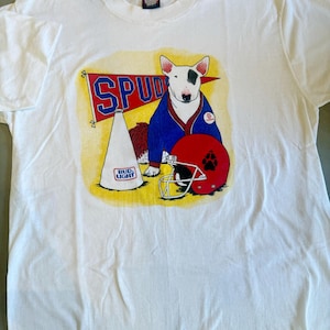 May include: White t-shirt featuring a cartoon Bull Terrier wearing a blue jacket and a red football helmet. The shirt also displays a banner that says "SPUD" and a Bud Light megaphone.