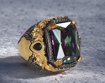 May include: A gold ring with a large, rectangular, iridescent gemstone set in a black metal setting. The ring has intricate details and a black stone on the side.