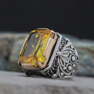 May include: A silver ring with a large, yellow gemstone set in a gold bezel. The ring has intricate, black filigree detailing around the stone.