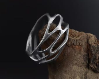 Può includere: Un anello d'argento con un design geometrico traforato. L'anello è realizzato in un unico pezzo di metallo e ha una finitura liscia e lucida.