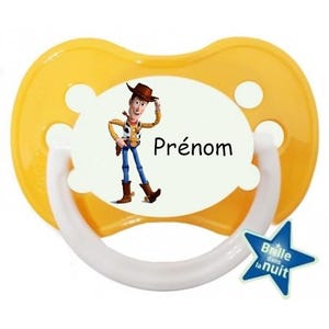 Peut inclure: Sucette jaune avec une poignée blanche et un insert ovale blanc représentant un dessin animé de Woody de Toy Story. L'insert ovale porte le texte "Prénom". Une petite étoile avec le texte "Brille dans la nuit" se trouve dans le coin inférieur droit.