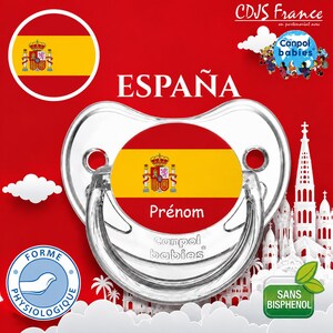 Pode incluir: Uma chupeta de plástico transparente com um inserto central circular exibindo a bandeira espanhola e a palavra Prénom impressa em branco. A chupeta inclui o logótipo Canpol babies, um ícone de forma fisiológica e uma etiqueta verde sans bisphénol.