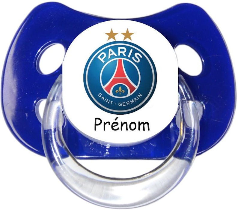 May include: A blue pacifier featuring a circular white center with the Paris Saint-Germain football club logo, two gold stars above the crest, and the word Pr&eacute;nom printed in black text below the circular emblem on the front of the pacifier.