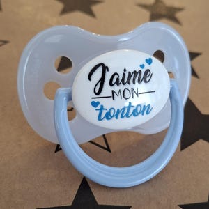 May include: A light blue pacifier with a white round disc that says "J'aime mon tonton" with two blue hearts.