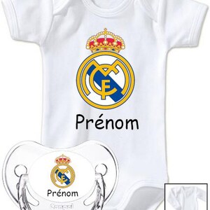 May include: White baby onesie and pacifier set featuring the Real Madrid logo in yellow, blue, and red. The word "Pr&eacute;nom" is printed in black on both items. The pacifier is clear with the brand name "Canpol babies".