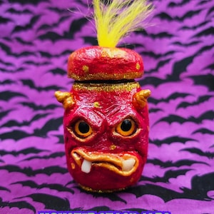May include: A red monster-themed stash jar with yellow hair and gold accents. The jar has a detailed face with horns, eyes, and teeth. Text on the jar reads "MINI JARSTERS" and "MONSTER STASH JARS BY LIVING DEAD GIRL NICOLE".