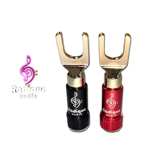 May include: Two gold-plated speaker wire banana plugs with red and black plastic bodies. The plugs are labeled "Radique Audio" with a treble clef logo.