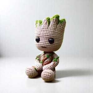 May include: A crocheted plush toy of a character from the Guardians of the Galaxy movie, Groot. The toy is sitting with its legs crossed and has a green leafy head and brown roots.