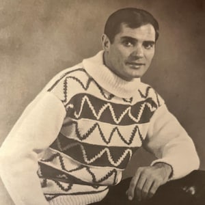 May include: A black and white photo of a man wearing a white turtleneck sweater with a black and white geometric pattern. He is sitting with his hands in his lap.