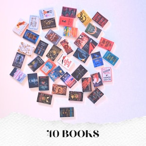 May include: A collection of 40 miniature books with various titles and colorful covers, arranged on a white and pink surface. The books are of different sizes and shapes, with titles such as "Morning Star" and "The Plot". The text "40 BOOKS" is at the bottom.