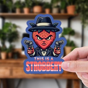May include: A sticker depicting a cartoon strawberry with an angry face, wearing a fedora and pinstripe suit, holding two pistols. The text "THIS IS A STROBBERY" is displayed in red and blue.