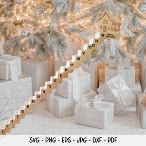 Op de afbeelding: Een houten adventskalender in de vorm van een trap, genummerd van 1-25, met een klein huisje bovenaan. De kalender staat tegen een achtergrond van ingepakte cadeaus en een versierde kerstboom. Het huisje heeft de tekst "Merry Christmas".
