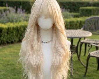 May include: A long, wavy, platinum blonde wig with bangs styled on a mannequin head. The wig features a center part and soft, flowing layers that cascade down the shoulders. A delicate necklace with small, multicolored circular beads is visible.