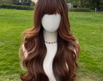 May include: A long, wavy wig with a dark brown base and lighter brown highlights. The wig features a full fringe and is styled on a mannequin head. A colorful beaded necklace is worn around the mannequin's neck.