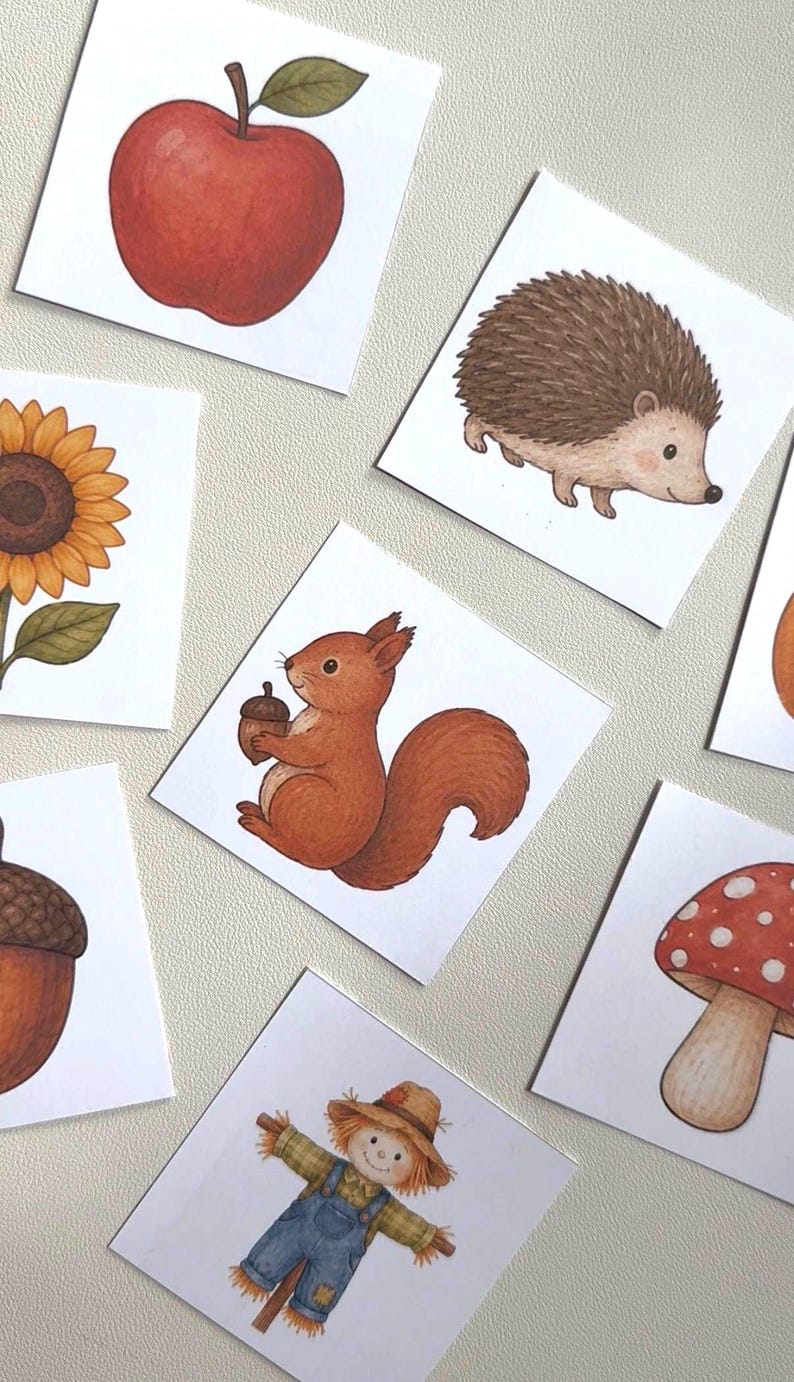 May include: A collection of square cards featuring illustrations of a red apple, a brown hedgehog, a yellow sunflower, a brown squirrel holding an acorn, a large brown acorn, a red and white spotted mushroom, and a scarecrow in blue overalls.
