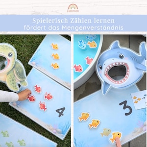 May include: Educational counting game featuring a sea turtle and shark with open mouths, light blue boards with printed numbers, and small colorful fish tokens. The text reads: "Spielerisch Z&auml;hlen lernen f&ouml;rdert das Mengenverst&auml;ndnis."