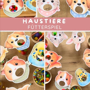 Op de afbeelding: Een set dierenthema voerspel-uitsparingen met illustraties van een cavia, kat, hond, konijn, goudvis en parkiet, elk met een ronde mondopening. De tekst HAUSTIERE FÜTTERSPIEL wordt in het wit weergegeven op een roze achtergrond.