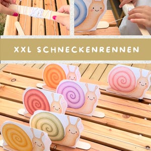 Op de afbeelding: Een slakkenrace-spelset met meerdere kartonnen slakkenfiguren in oranje, roze, rood, paars, groen en geel, elk bevestigd aan een houten stokje. De set bevat wit touw voor de race en de tekst XXL SCHNECKENRENNEN.