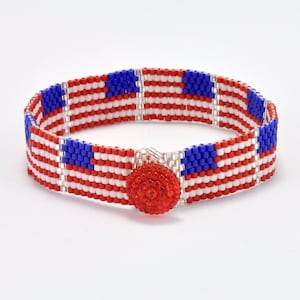 Puede incluir: Un brazalete de cuentas rojo, blanco y azul con un cierre de botón rojo. El brazalete está diseñado para parecerse a la bandera estadounidense.