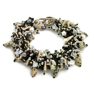 May include: A multi-strand bracelet featuring a mix of black, white, and brown beads, including small pearls, crystal beads, and dalmatian jasper beads. The bracelet has a silver toggle clasp.