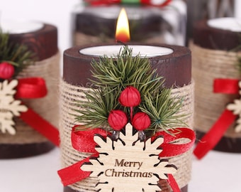 May include: Set of four brown wooden candle holders decorated with burlap twine, red ribbon, and a wooden snowflake with the text "Merry Christmas". Each holder has a small green pine sprig and red berries.