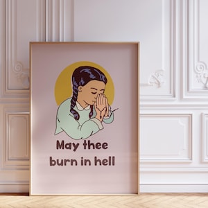 Puede incluir: Impresión artística enmarcada con una ilustración de dibujos animados de una niña con trenzas, con las manos juntas en oración, sobre un círculo amarillo. El texto "May thee burn in hell" está impreso debajo en letras marrones.