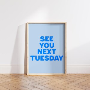 May include: A light blue framed poster with the text "SEE YOU NEXT TUESDAY" in bold blue letters.